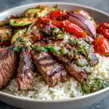 In a topped Grilled Steak Bowl, juicy steak slices rest on fluffy rice next to roasted zucchini, peppers, and onions.