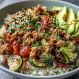 A steaming Ground Turkey Bowl with seasoned meat, broccoli, and avocado slices, topped with fresh cilantro and lime wedges.