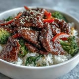 Juicy slices of beef in glossy teriyaki sauce served over steamed rice with colorful sautéed vegetables.