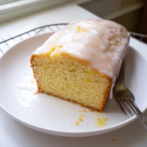 Golden-brown Lemon Pound Cake with a crackled top and glistening lemon glaze on a white plate, ready to slice.