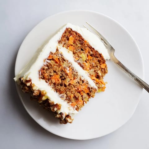 Moist Carrot Cake slice on a plate, with creamy frosting and a cup of coffee nearby.