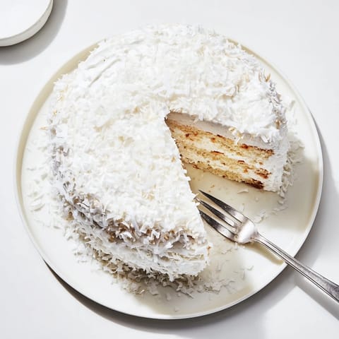 A moist coconut cake slice reveals luscious coconut filling between tender white layers, ideal for an afternoon tea or celebration.