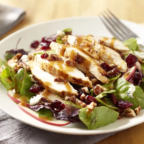 Autumn-inspired Caramel Apple Chicken Salad features vibrant red onions, dried cranberries, and a drizzle of caramel-pecan dressing over a bed of arugula and romaine.  