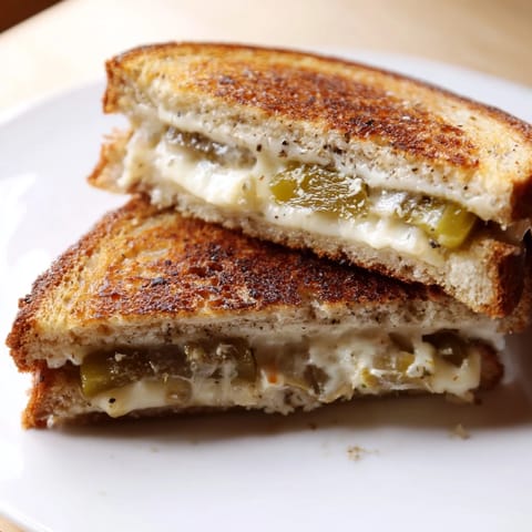Golden brown Jalapeño Pepper Jack Grilled Cheese slices reveal melted cheese and tangy pickled jalapeños on a rustic cutting board.  