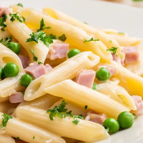 Steaming Spring Pea & Ham Pasta served on a rustic wooden table, garnished with fresh parsley and grated Parmesan cheese.