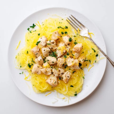 Golden roasted spaghetti squash strands topped with tender lemon-garlic chicken pieces and fresh parsley garnish, glistening with pan sauce.