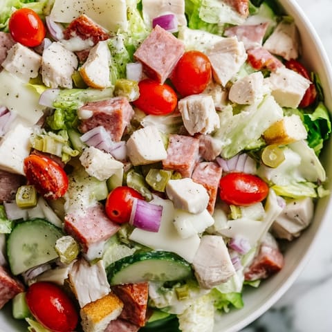 A close-up of Italian Deli Chopped Chicken Salad featuring tender chicken, salami, and provolone on crisp romaine with cherry tomatoes, pepperoncini, and a zesty herb dressing.
