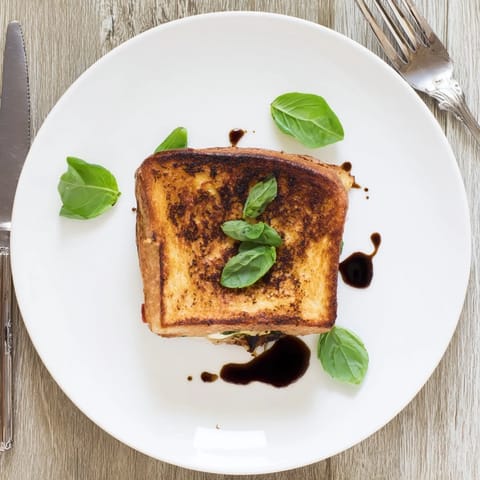 A close-up of a Roasted Veggie Caprese Grilled Cheese, with melted mozzarella stretching from toasted bread layered with roasted veggies and basil.