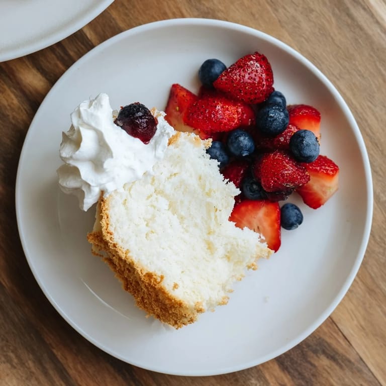 Light and airy Angel Food Cake served with a vibrant mixed berry compote and a dollop of cream.