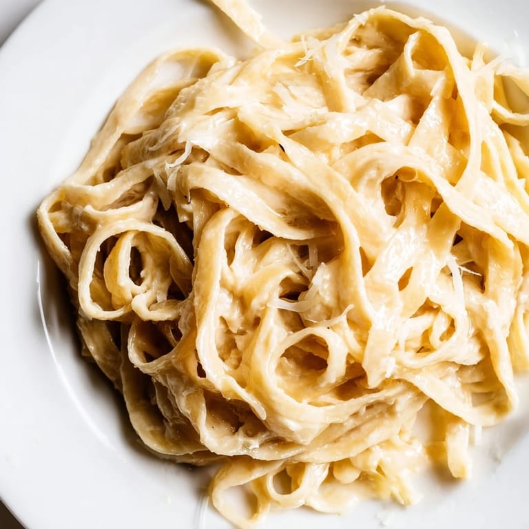 In a shallow bowl, Roasted Garlic Cream Pasta is served with extra Parmesan and a sprig of parsley on top.