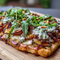 Grilled flatbread topped with sweet peaches, melted Brie, and BBQ sauce, garnished with fresh basil and arugula.